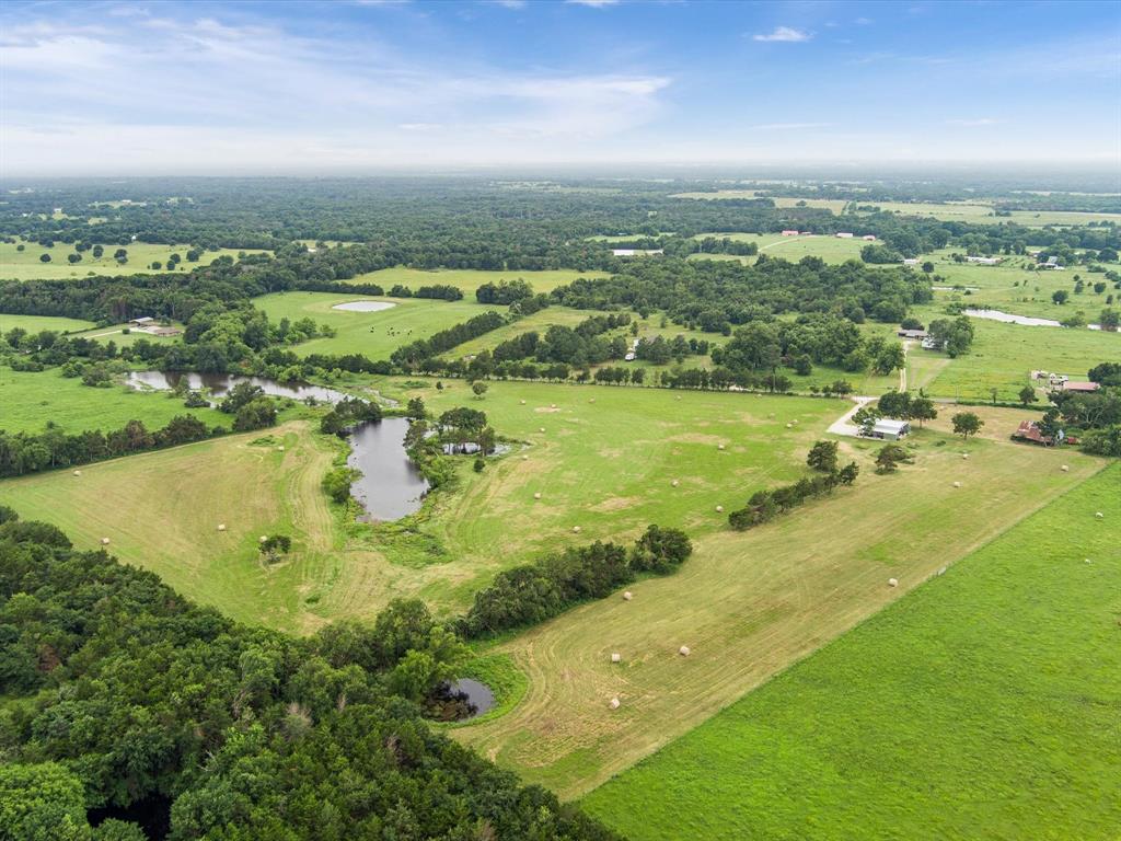 Aerial view of a lush landscape featuring ponds, green fields, trees, and a under a partly cloudy sky.