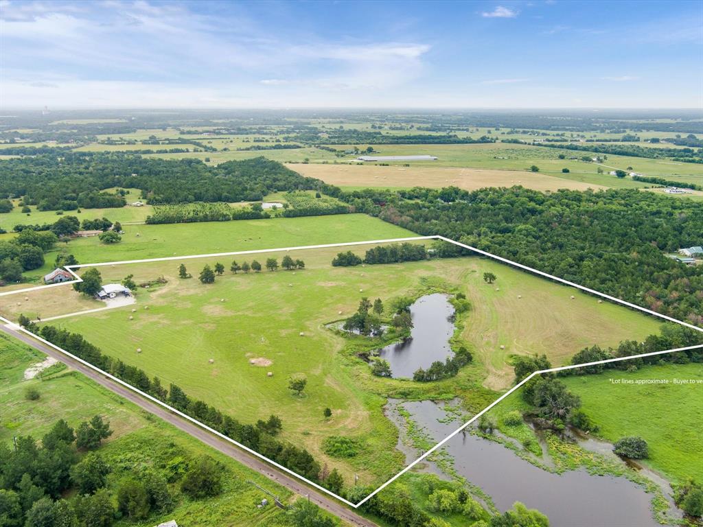 Aerial view of a lush green landscape with fields, trees, ponds, and hay bales under a cloudy sky.