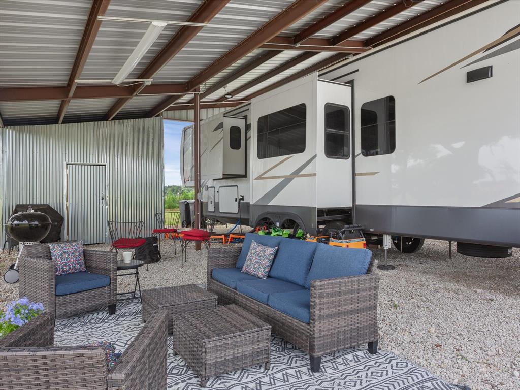 Another covered outdoor living area under a metal shelter, adjacent to the parked recreational vehicle (RV), in a rural setting.