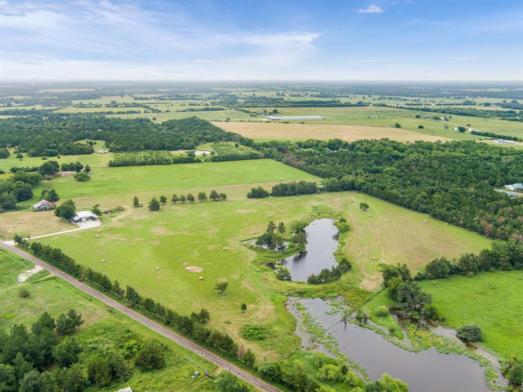 Aerial view of a rural landscape with fields, trees, 3 ponds, buildings, under a cloudy sky.