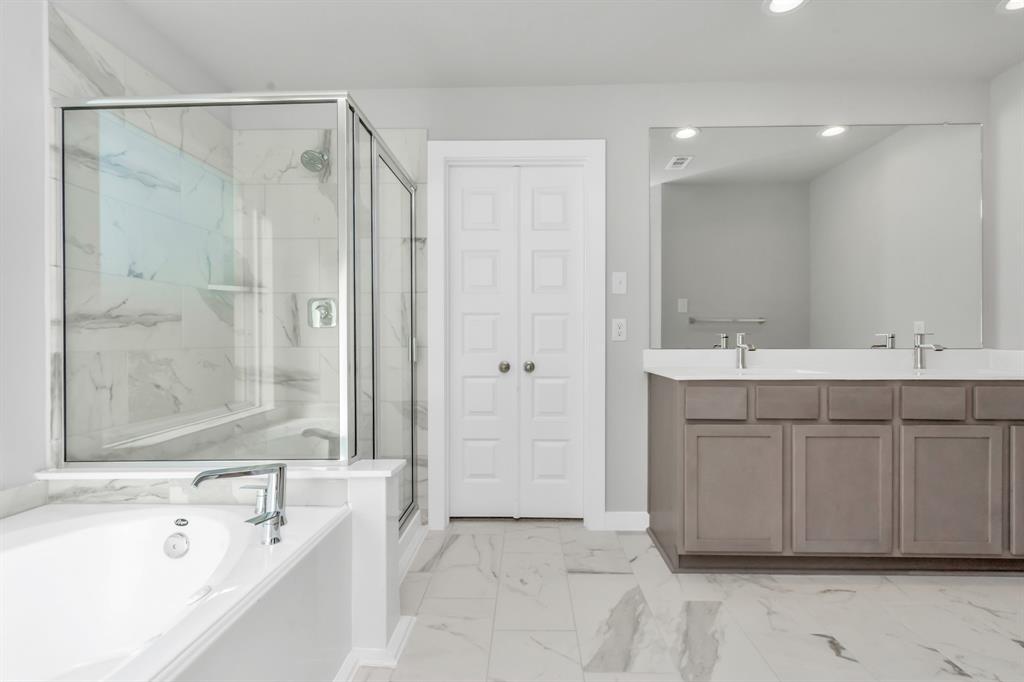 Indulge in a spa-like retreat within the confines of this primary bathroom. Delight in a spacious walk-in shower enveloped in stylish tile surround, unwind in a separate garden tub adorned with custom detailing, and elevate your daily routine at the elegant vanity, now equipped with double sinks, light countertops, modern hardware, and bright recessed lights. Sample photo of completed home with similar floor plan. As-built interior colors and selections may vary.