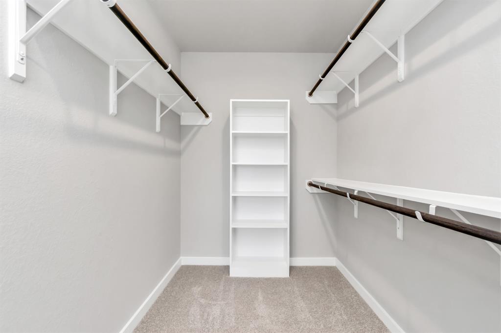 Experience luxury in this spacious walk-in closet with high ceilings and plush carpet. Warm paint tones, built-in shelving, and dark finishes create a contemporary and functional retreat. Sample photo of completed home with similar floor plan. As-built interior colors and selections may vary.