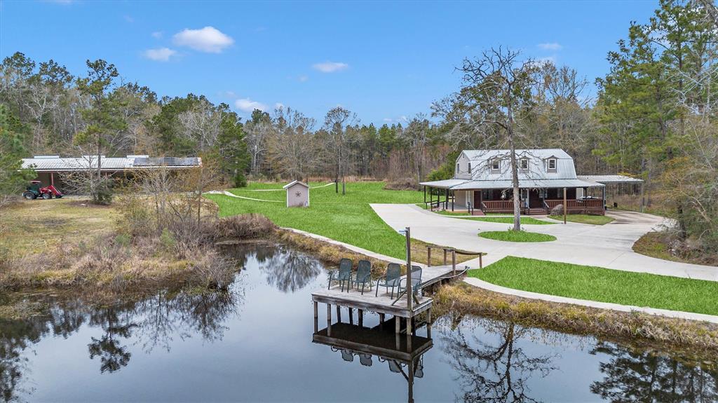 Experience serene country living near Lake Livingston in this expansive 22.39-acre property in Point Blank, Texas. The mostly wooded and scenic landscape features two fully stocked ponds with concrete walkways and a deer stand, offering abundant opportunities for outdoor enthusiasts. The charming 4-bedroom, 2-bathroom home boasts a cozy wood stove and a wrap-around porch, perfect for relaxing and enjoying the natural surroundings. A 40x80 metal building, equipped with solar panels, includes a designated entertainment area complete with a bathroom, kitchen, and theater room, ideal for hosting gatherings. The property ensures privacy and security with its gated entrance, making it a true retreat for those seeking tranquility and modern amenities.