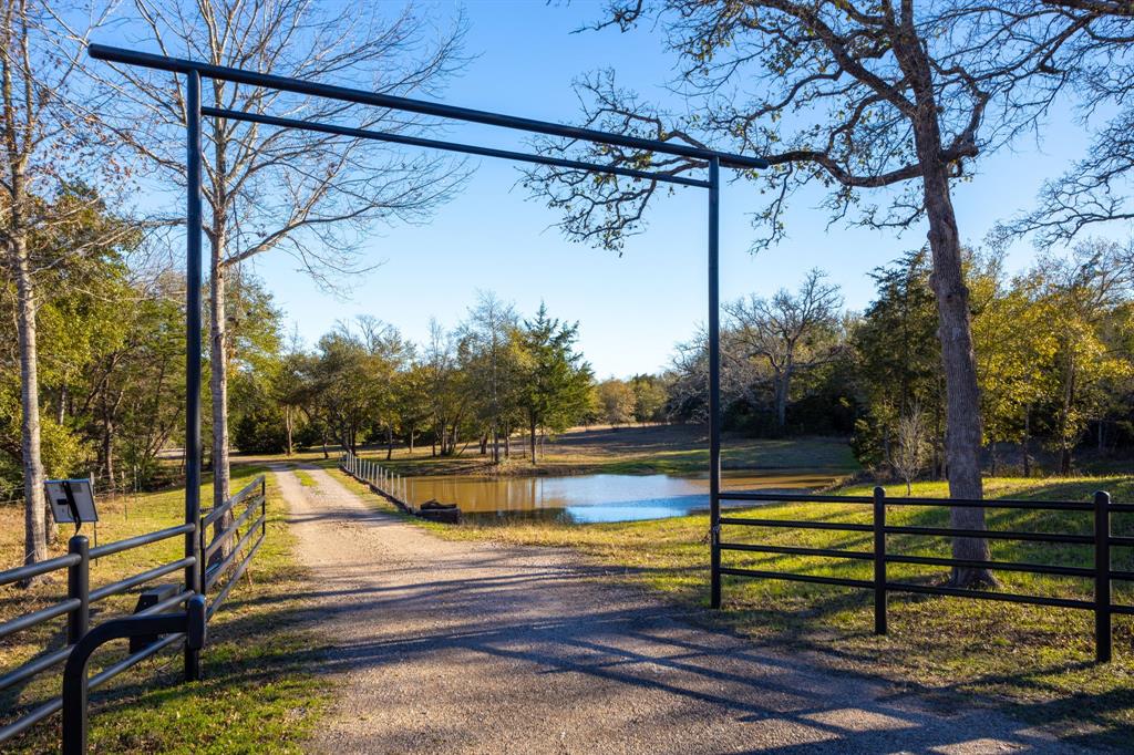 Escape to the tranquility of this 3-bedroom, 2.5-bath barndominium on 6.93 secluded, ag-exempt acres. Built in 2018, this 1,790 sq. ft. home offers an open-concept design with a spacious kitchen featuring granite countertops and an island, perfect for entertaining. The primary suite upstairs boasts a custom walk-in shower and double vanity. A laundry/mud room with a half bath adds convenience. The property features mature trees, a serene pond, and an automatic gated entry. Attached is a 40x40 shop with double roll-up doors and a 20x40 carport, offering ample space for projects and parking. Peaceful country living at its best!