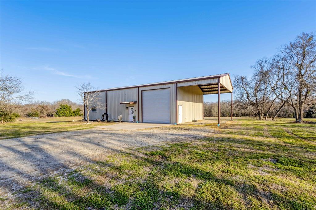 Escape to tranquility with this exceptional barndominium nestled on 20.5 unrestricted acres,  A true country gem, this property offers a blend of modern comfort and rustic charm. Boasting 3 spacious bedrooms and 2.5 bathrooms, this home features-stained concrete floors, adding durability, soaring 20 ft ceiling featuring tongue and groove to enhance the aesthetic. The kitchen is a chef's dream, complete with granite countertops, black stainless appliances and oversized island. For those with a passion for projects, the attached 35x20 garage with a 16-20 foot ceiling is ideal for work or hobbies. The 35x15 RV overhang provides protection for your recreational vehicles, while a 30x40 lean-to storage area adds even more versatility. Nature lovers will love the heavily wooded land, adorned with pecan and oak trees, creating a serene and private setting. The property is teeming with wildlife, including white-tailed deer and wood ducks. A 1/4-acre wooded pond is stocked with black bass,