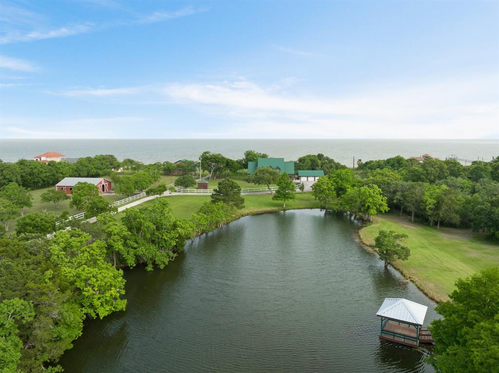 Custom craftsmanship, sweeping bay views & wide-open Texas skies define this one-of-a-kind legacy estate. Meticulously built w/enduring quality & pride, this 14 acre bay front property is a rare find. A true 8'' D Log cabin surrounded by serene views of the surrounding acreage, dual primary suites+2 secondaries, premium finishes & high-efficiency systems throughout. Multiple porches & patios encourage indoor/outdoor living. Oversize 3-car garage. Guest house w/ 2 primaries & separate utilities, perfect for guests or multigenerational living. Equestrian-ready with 7 stalls, tack room, wash area & cross-fenced acreage, the property also includes a commercial-grade outbuilding ideal for workshop/business operations. Lovely pond features a gazebo w/water+electric. Close to major thoroughfares including I-10, 99, and 225 and zoned to A-rated Barbers Hill ISD. Whether it be horses, hobbies, or homesteading, this property has all the infrastructure in place to live out your dreams.