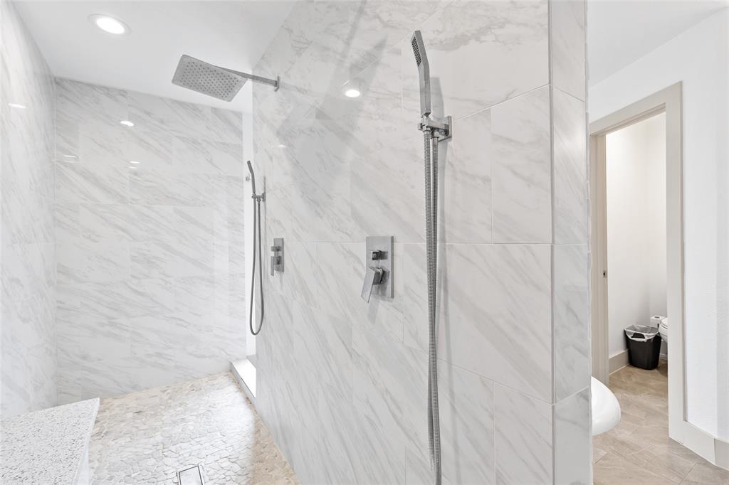 Your spacious walk-in shower is designed for both comfort and luxury, featuring elegant marble-look tile walls and a pebble stone floor. The built-in bench adds a relaxing touch, while dual showerheads—one rainfall and one handheld—offer a spa-like experience.