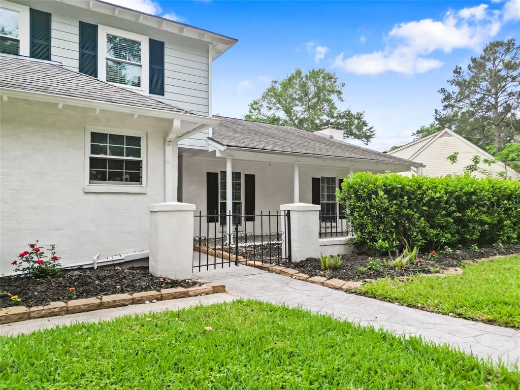 A closer look reveals your welcoming front entrance, framed by a decorative iron gate and bordered by neatly mulched flower beds. Your covered front porch offers a shaded retreat, perfect for morning coffee or evening relaxation, while mature hedges enhance the sense of privacy. Subtle architectural details and well-maintained landscaping provide a polished and inviting look right from the curb.