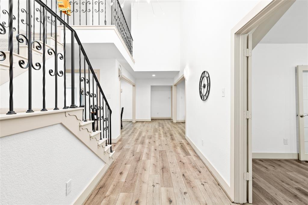 Your stunning entryway welcomes you with grand ceilings and a dramatic open-air second level, creating an immediate sense of space and light. The wrought iron staircase railing adds sophistication and architectural detail, while the warm-toned, wide plank flooring brings cohesion and flow throughout the lower level. Clean lines and neutral tones provide a versatile canvas ready for any design style.