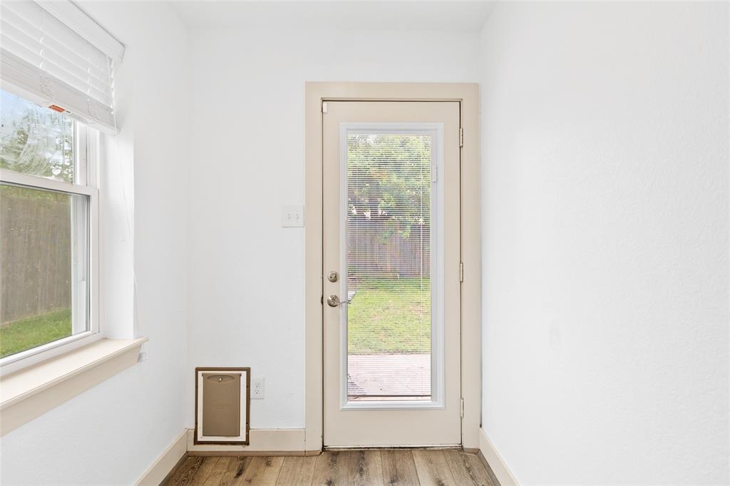 This bright and functional back entryway features a full glass door with built-in blinds, providing easy access to the backyard while letting in plenty of natural light. A nearby window enhances the airy feel, and a built-in pet door at the base offers added convenience for furry family members. Durable wood-look flooring completes the space with warmth and practicality.