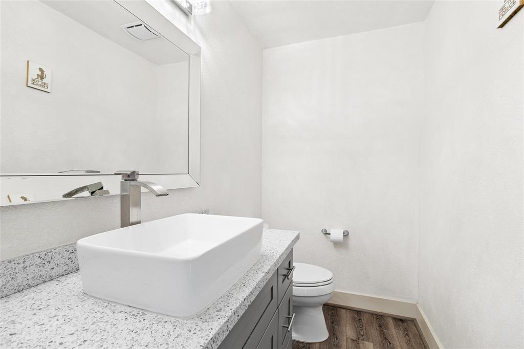 Conveniently located just off the kitchen, your half bath offers a modern design with a square vessel sink on a speckled quartz vanity, paired with a chrome faucet for a clean, refined look. A large framed mirror enhances the sense of space, while neutral tones and wood-look flooring create a warm, welcoming atmosphere. It's a practical and stylish space, perfect for guests or quick use.