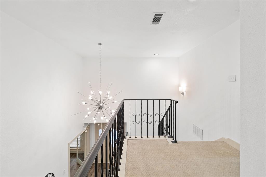 Your upper-level landing is bathed in natural light, creating an open, welcoming transition space. A striking modern chandelier adds a bold touch to the stairwell, while classic wrought-iron railings and soft neutral carpeting enhance the area’s charm. This versatile space is ideal for a cozy reading nook or as a place for decorative accents, offering both function and style.