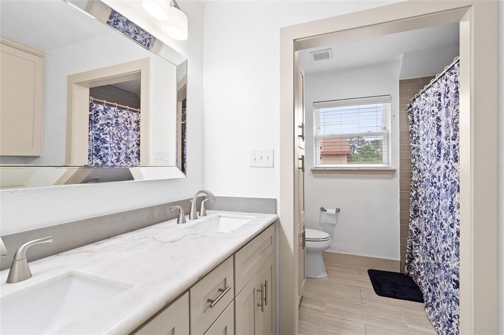 Your upstairs full bathroom features a spacious double-sink vanity with a marble-style countertop and brushed nickel fixtures, creating a modern and polished look. The separate water closet is filled with natural light through a window, while the tiled tub-shower combo adds functionality and style. With ample cabinetry for storage, this bathroom is perfect for shared use or guests.