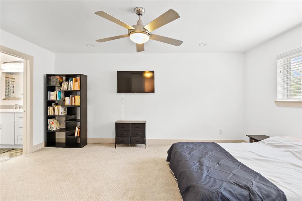 This spacious upstairs en-suite bedroom is ideal for in-laws or guests, featuring plush carpeting and a large window that fills the room with natural light. Neutral tones and recessed lighting create a bright atmosphere, while the ceiling fan ensures comfort year-round. Direct access to a full bathroom adds convenience, and the layout is easily adaptable.