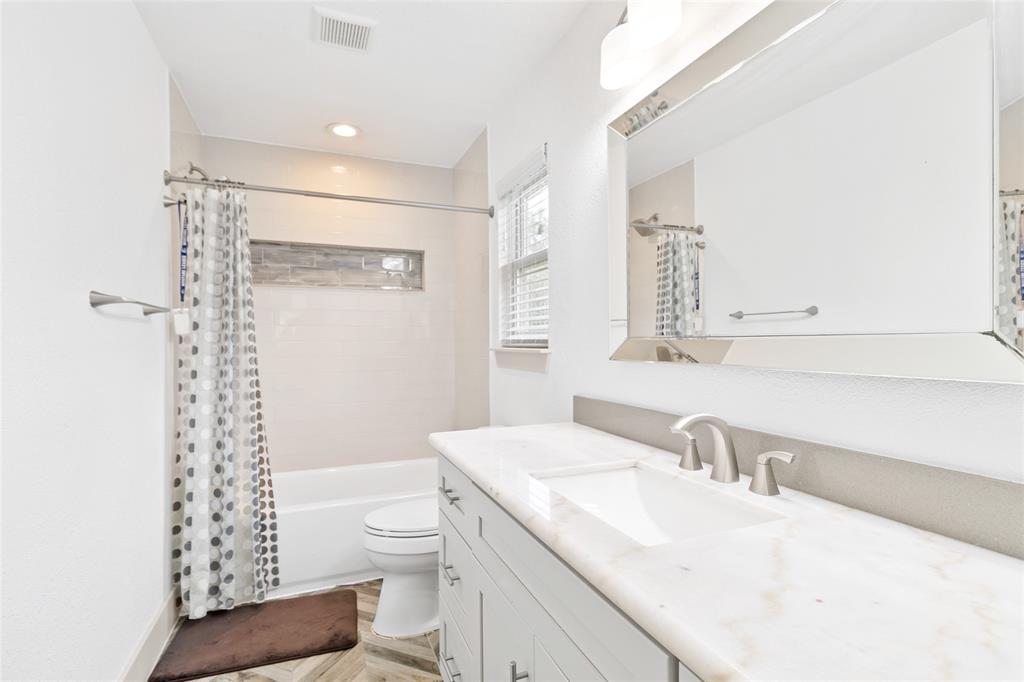 Your upstairs ensuite bathroom features a spacious vanity with an elegant stone countertop and a wide framed mirror. The tub-shower combo boasts contemporary tilework and a stylish accent niche, all bathed in natural light.