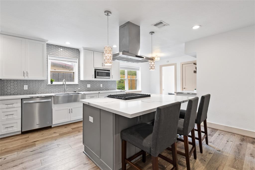Welcome to your modern kitchen, featuring a sleek waterfall-edge quartz island—perfect for prepping or entertaining. A bold hex tile backsplash adds style, while stainless steel appliances and a deep farmhouse sink offer function. Pendant lighting and ample cabinetry complete this polished, organized space.
