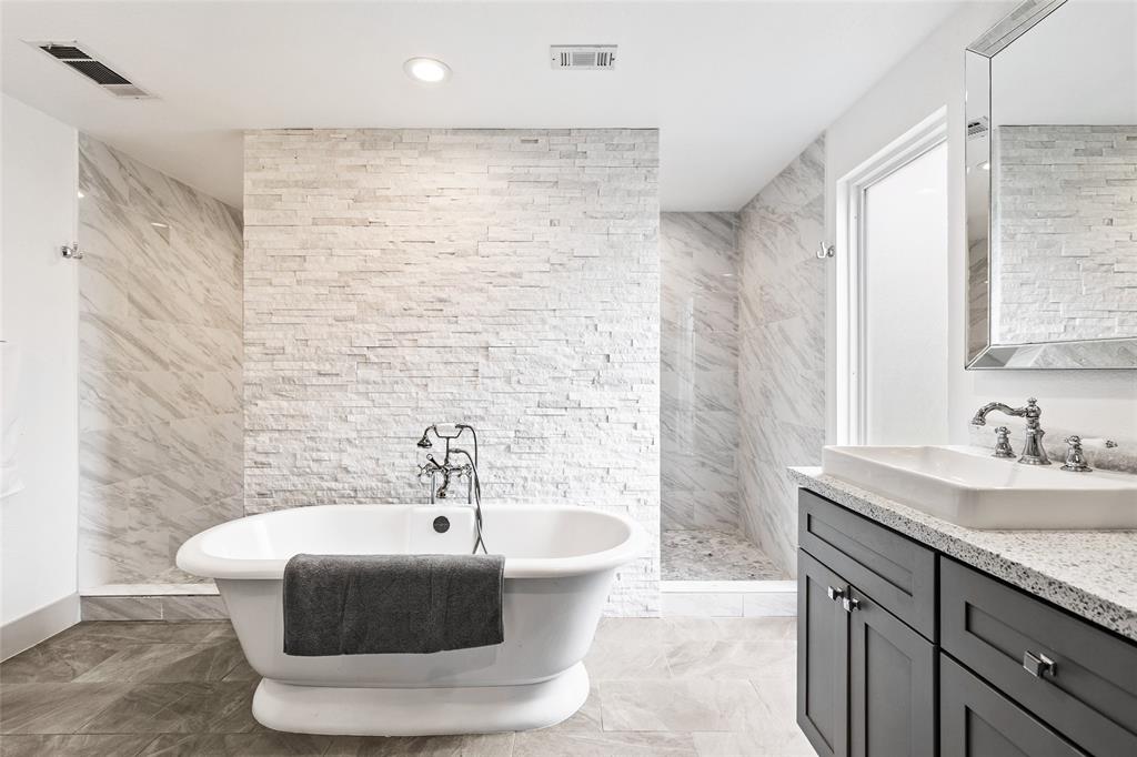 Your elegant bathroom combines comfort and style, featuring a freestanding soaking tub set against a textured white stone accent wall for a spa-like feel. The walk-in shower, wrapped in marble-style tile, adds a sleek touch, while the vanity with a quartz countertop and modern fixtures offers both function and flair.