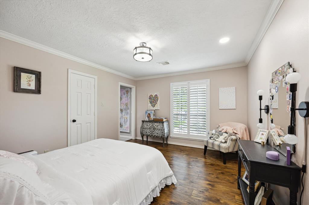 This bedroom features a cozy and bright space with hardwood floors, a large window with shutters, and a modern light fixture. It includes a comfortable bed, a stylish vanity, and a cozy chair, offering both functionality and charm.
