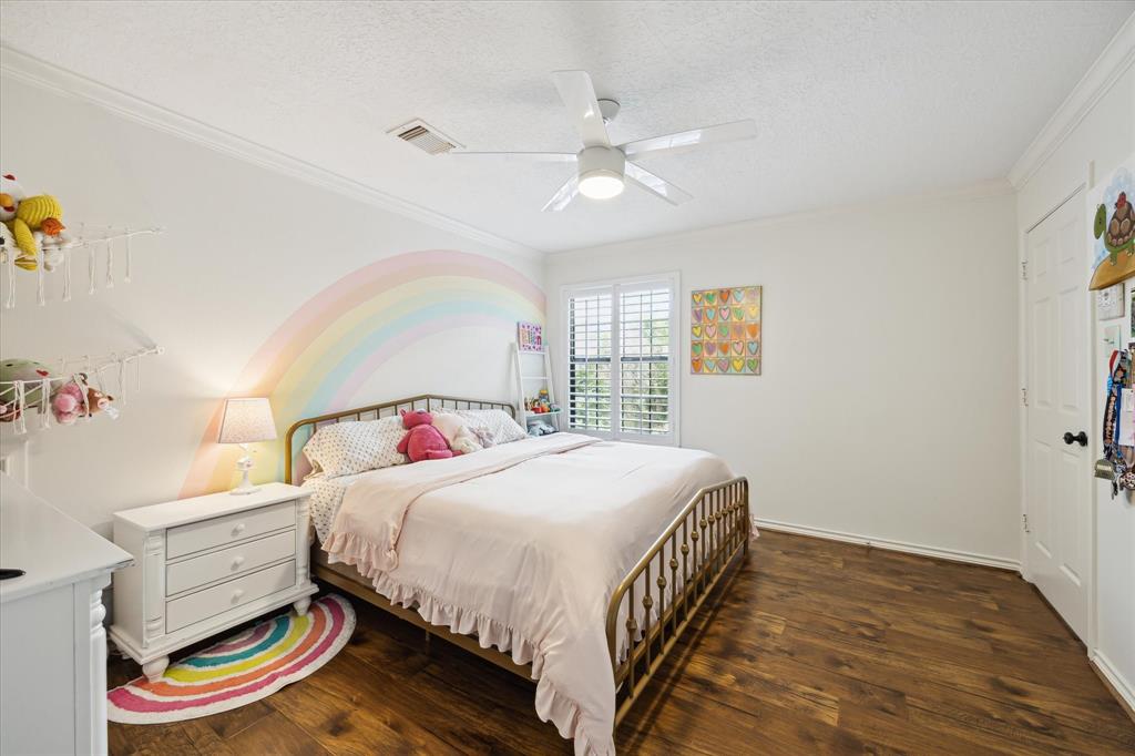 Bright and cheerful secondary bedroom featuring warm wood floors, crown molding, and plantation shutters. Including  a private vanity area with access to a Jack and Jill bathroom—perfect for shared use while maintaining personal space