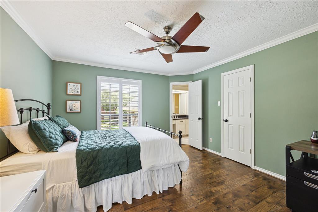 Charming guest bedroom with warm wood flooring, crown molding, and plantation shutters offering plenty of natural light. Features an en-suite bath access and generous closet space—ideal for guests or family members seeking comfort and privacy