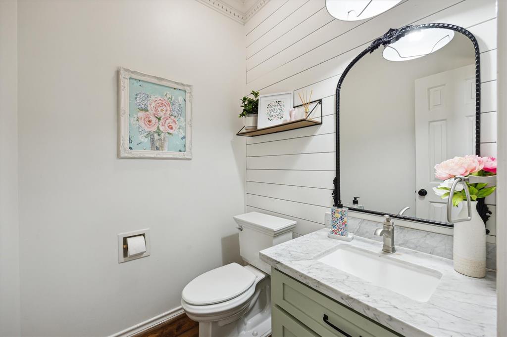 Charming first-floor half bath with designer touches, including shiplap accent wall, elegant framed mirror, upgraded marble vanity, and stylish fixtures. A beautifully refreshed space perfect for guests