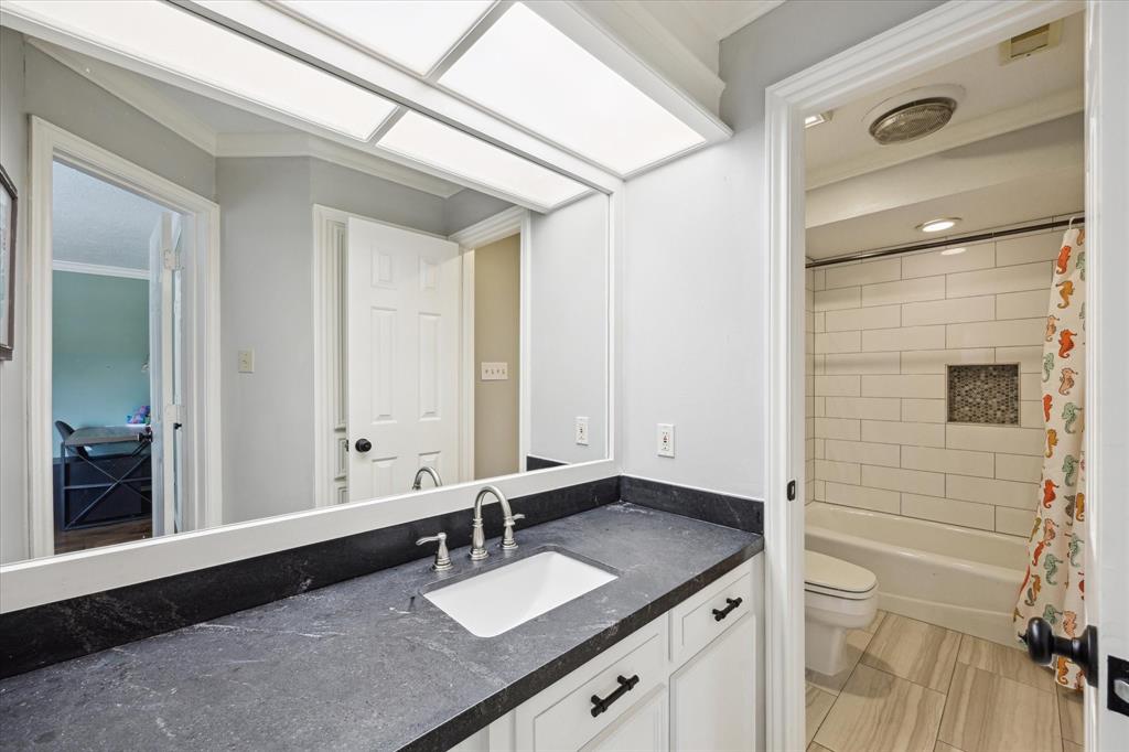 Upstairs full bathroom featuring a sleek vanity with black stone countertops, modern fixtures, and a tub/shower combo with stylish tile surround and niche. Conveniently located between the game room and a secondary bedroom—perfect for shared use or guests