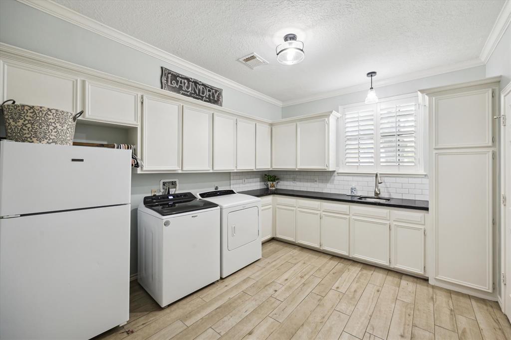 Well-appointed laundry room with ample cabinetry, wood-look tile, utility sink, and space for an extra fridge. Includes a convenient half bath—perfect for drying off after a swim in the pool