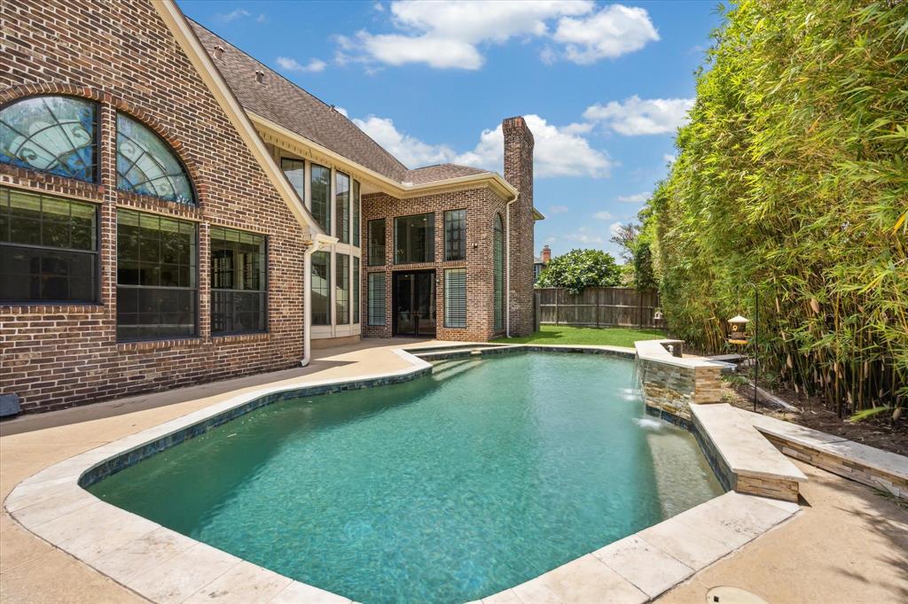 This stunning backyard features a spacious in-ground pool surrounded by a brick exterior and lush greenery, perfect for relaxation and entertaining. The large windows and architectural details of the house enhance the elegance and provide ample natural light.