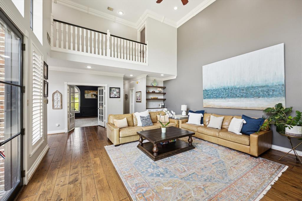 This spacious living room features high ceilings, a large loft area, and abundant natural light. It has elegant wood flooring, a cozy sectional sofa, and tasteful decor, creating a welcoming and stylish atmosphere.